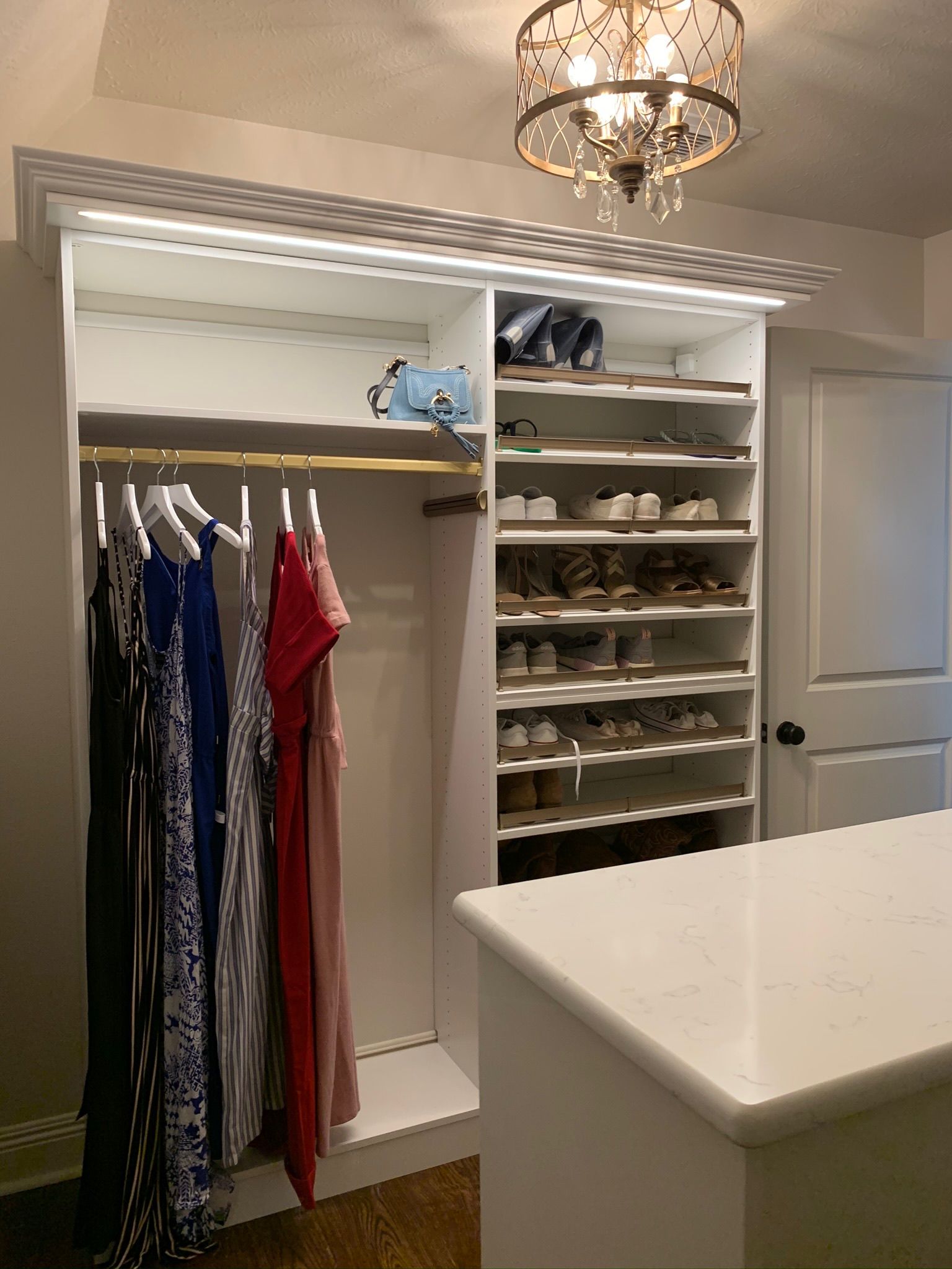 Walk-in closet with hanging clothes, shoe shelves, and a chandelier. A countertop is in the foreground.