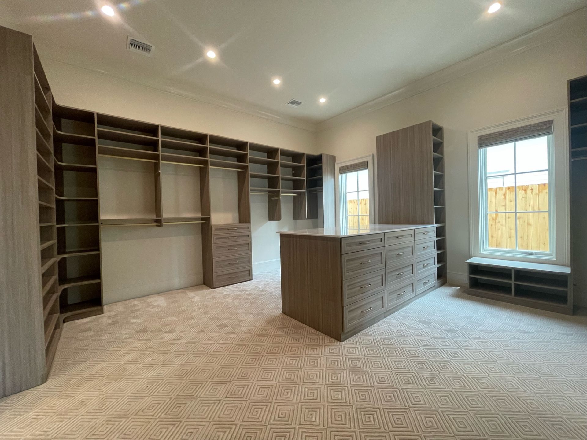 Spacious walk-in closet with shelves and drawers. Beige carpet, neutral-toned cabinetry, and a center island.