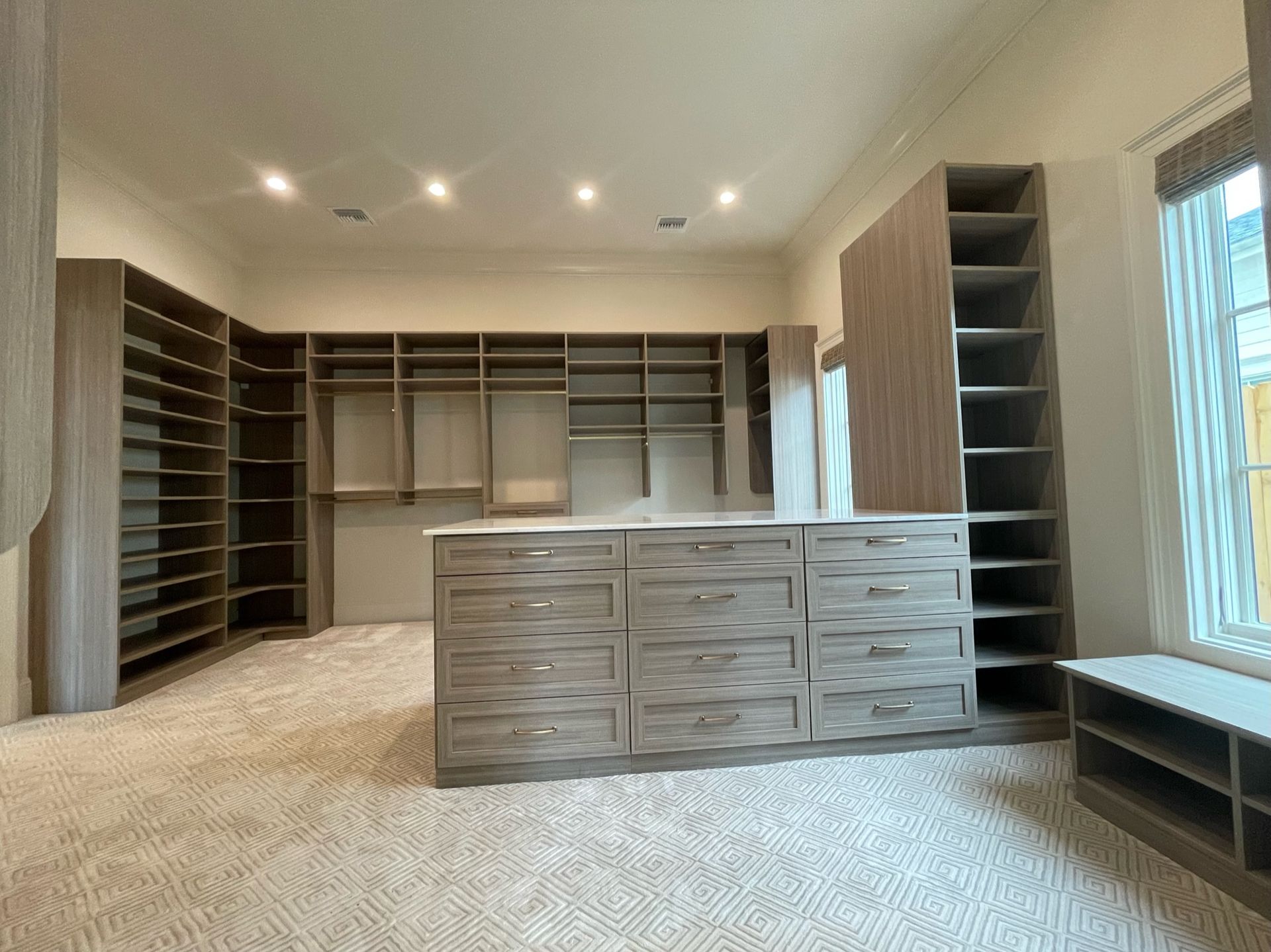 Spacious walk-in closet with built-in shelves and drawers, neutral tones, and a central island.