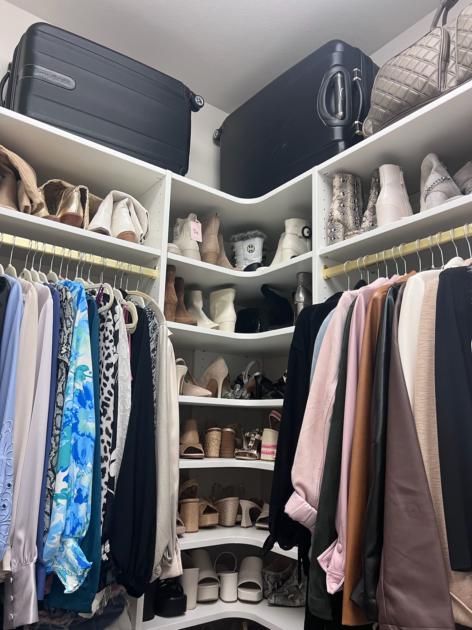 Walk-in closet with clothes hanging, shoe shelves, and suitcases on the top shelf.