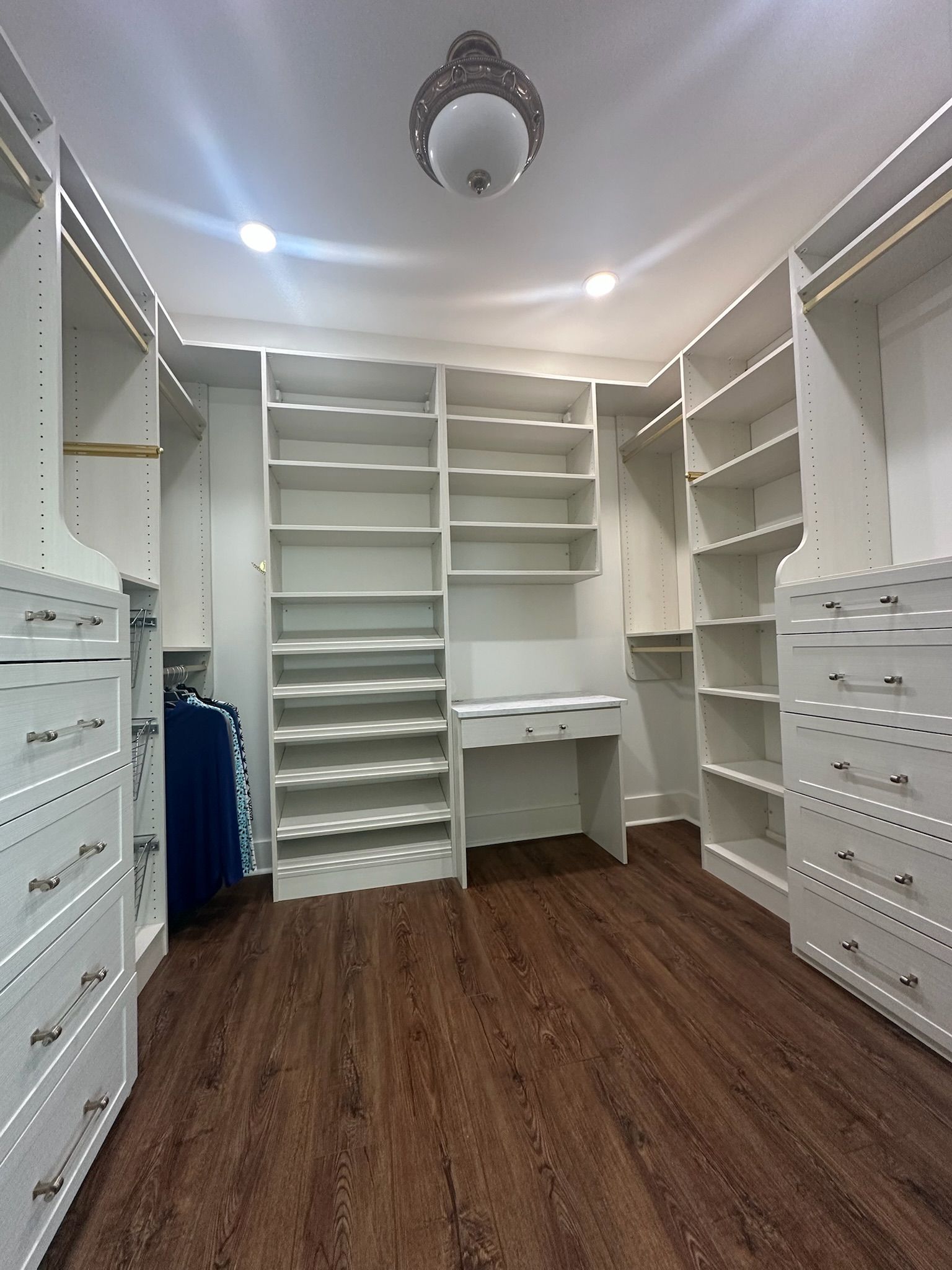 Walk-in closet with white shelves and drawers, wooden floors, and a desk.