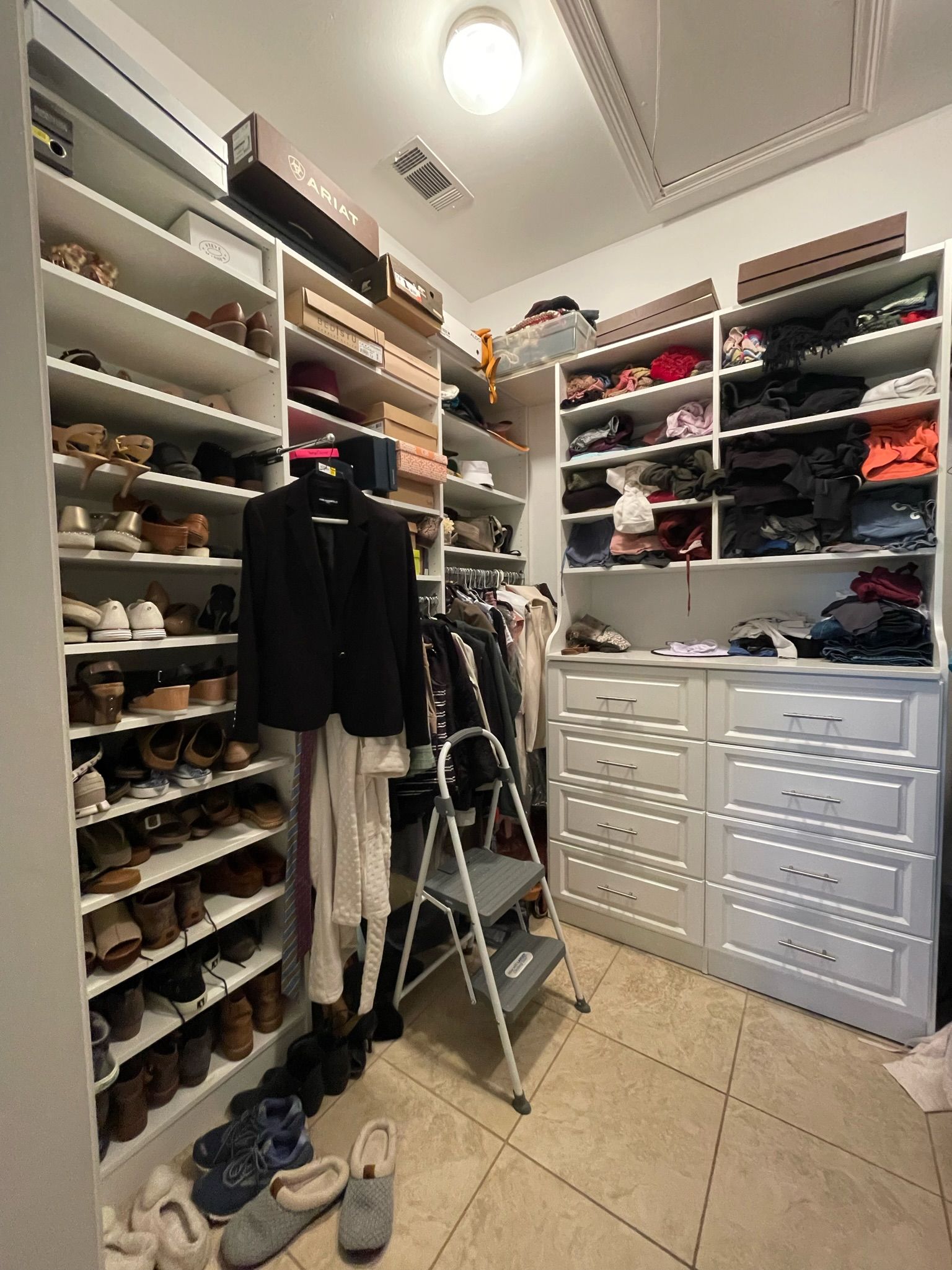 Walk-in closet with shelves of shoes, clothes, and drawers. A step ladder stands in the center.