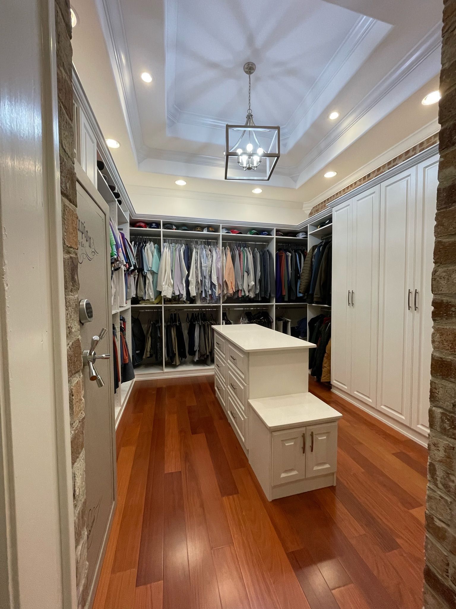 Walk-in closet with hardwood floors, white cabinetry, and hanging clothes. Center island and recessed lighting.