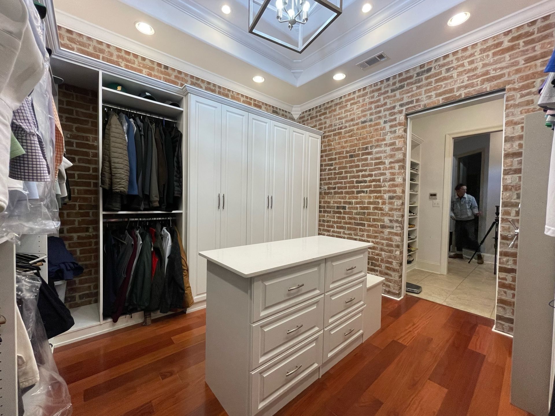 Walk-in closet with white cabinets, center island, brick wall, and a doorway.
