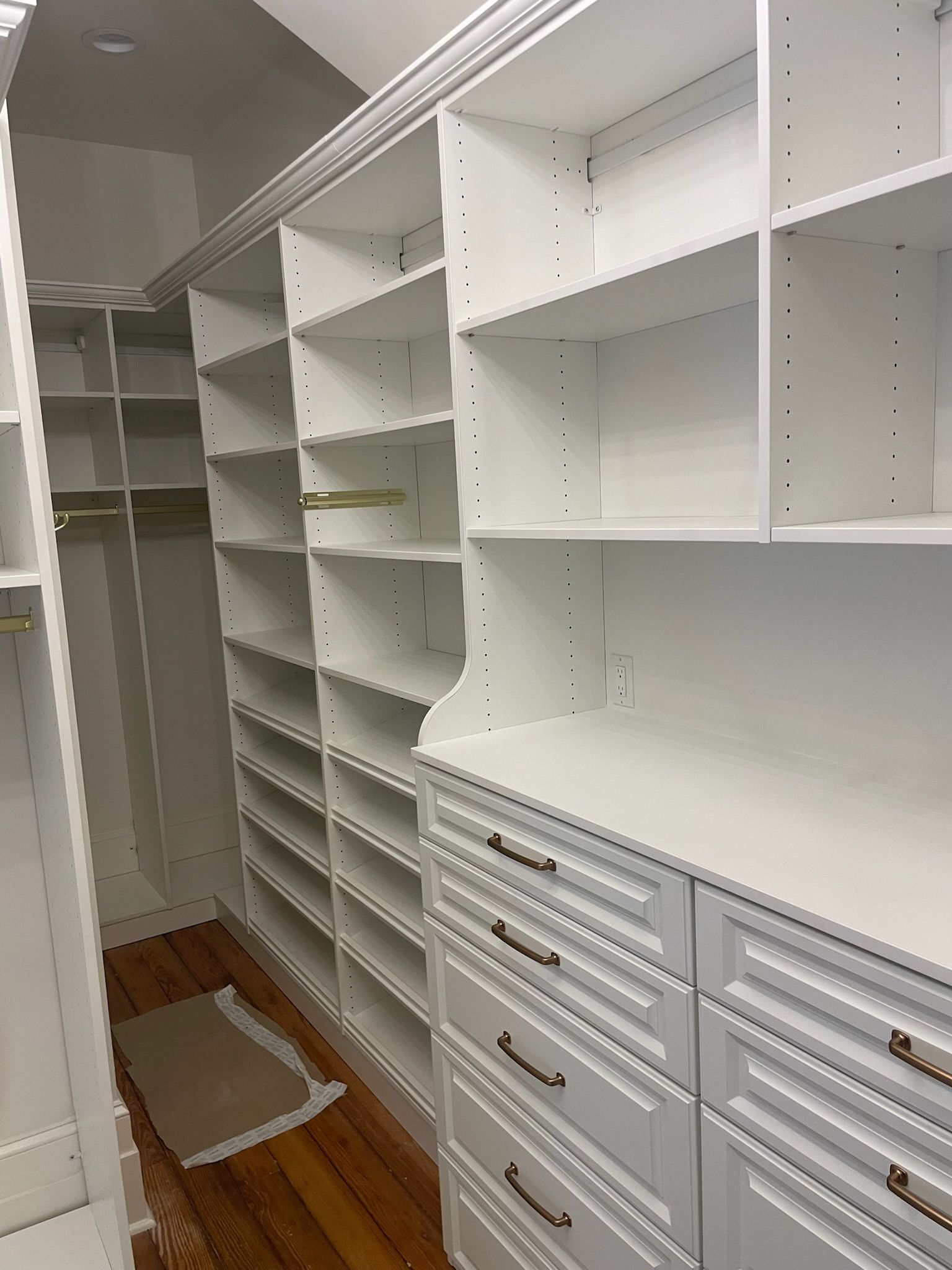 White closet shelving with drawers and rod, inside a walk-in closet with hardwood floors.