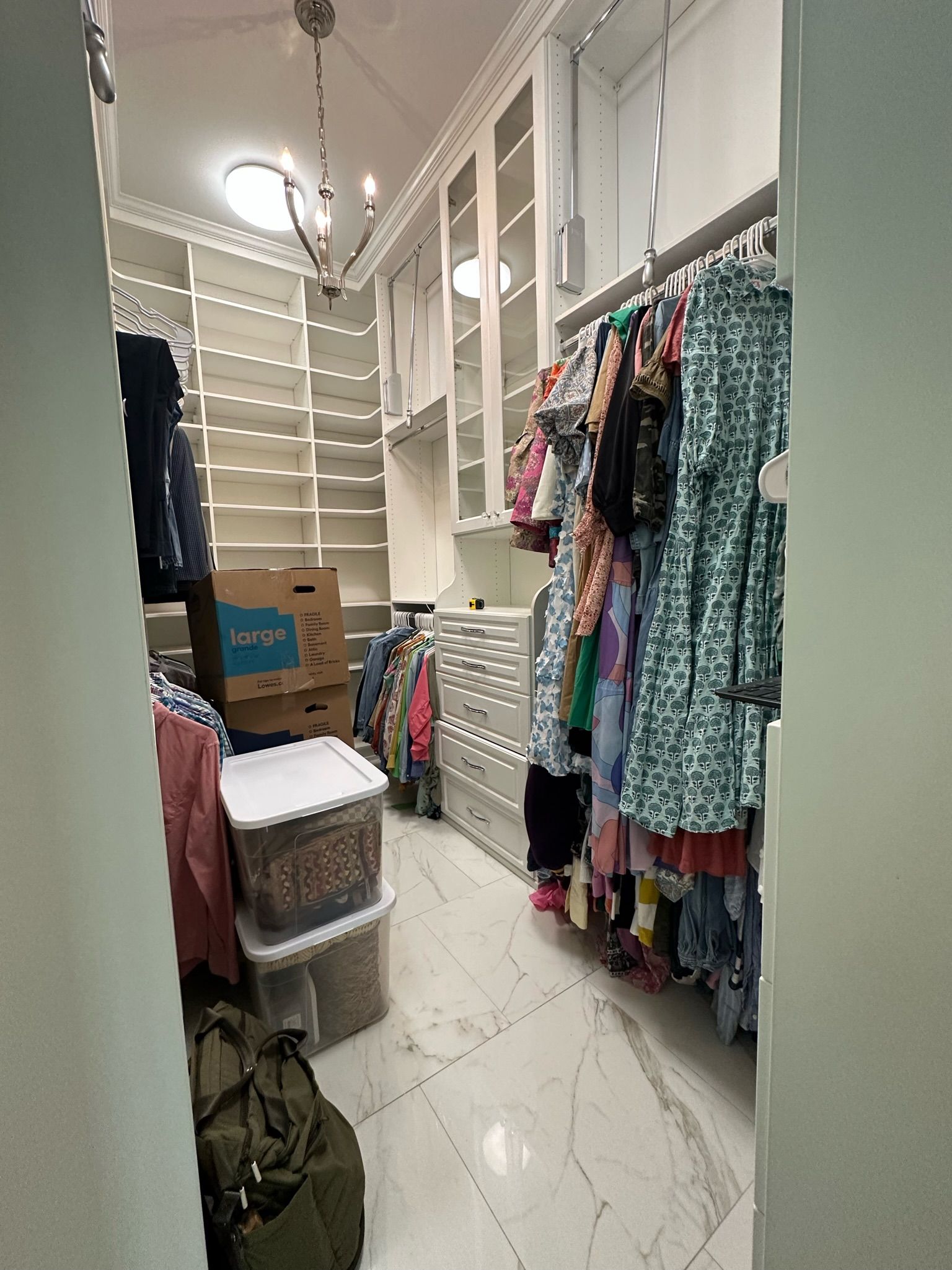 Walk-in closet with shelves and hanging clothes, cluttered with storage bins and a duffel bag, white and neutral tones.