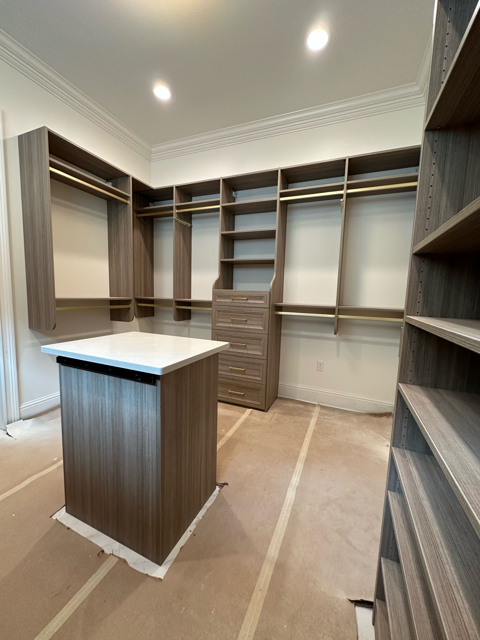 Walk-in closet with brown shelving and a central island. White walls, gold rods, and a white countertop.