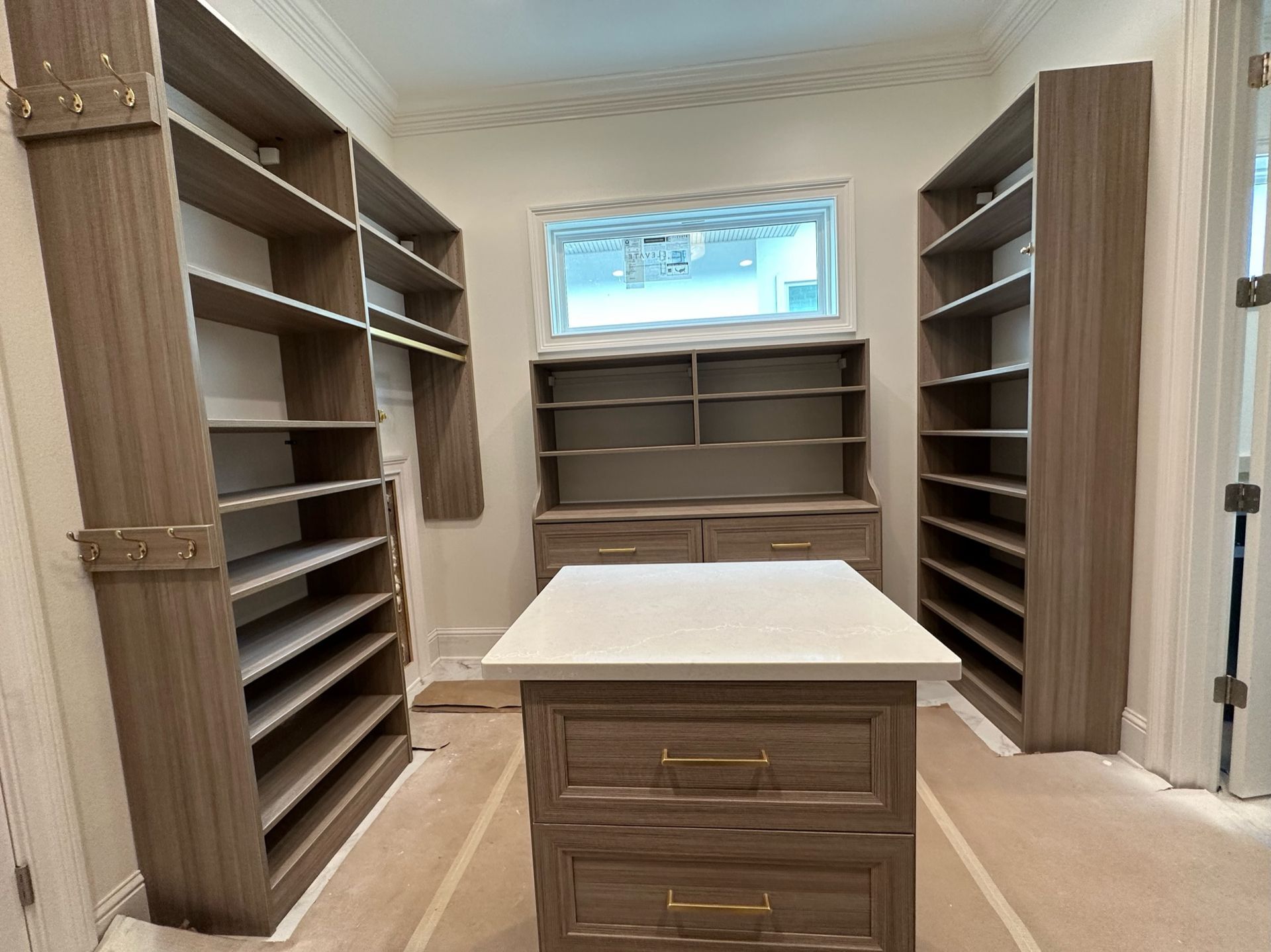 Walk-in closet with built-in shelves, drawers, and an island with a white countertop. Beige walls and flooring.