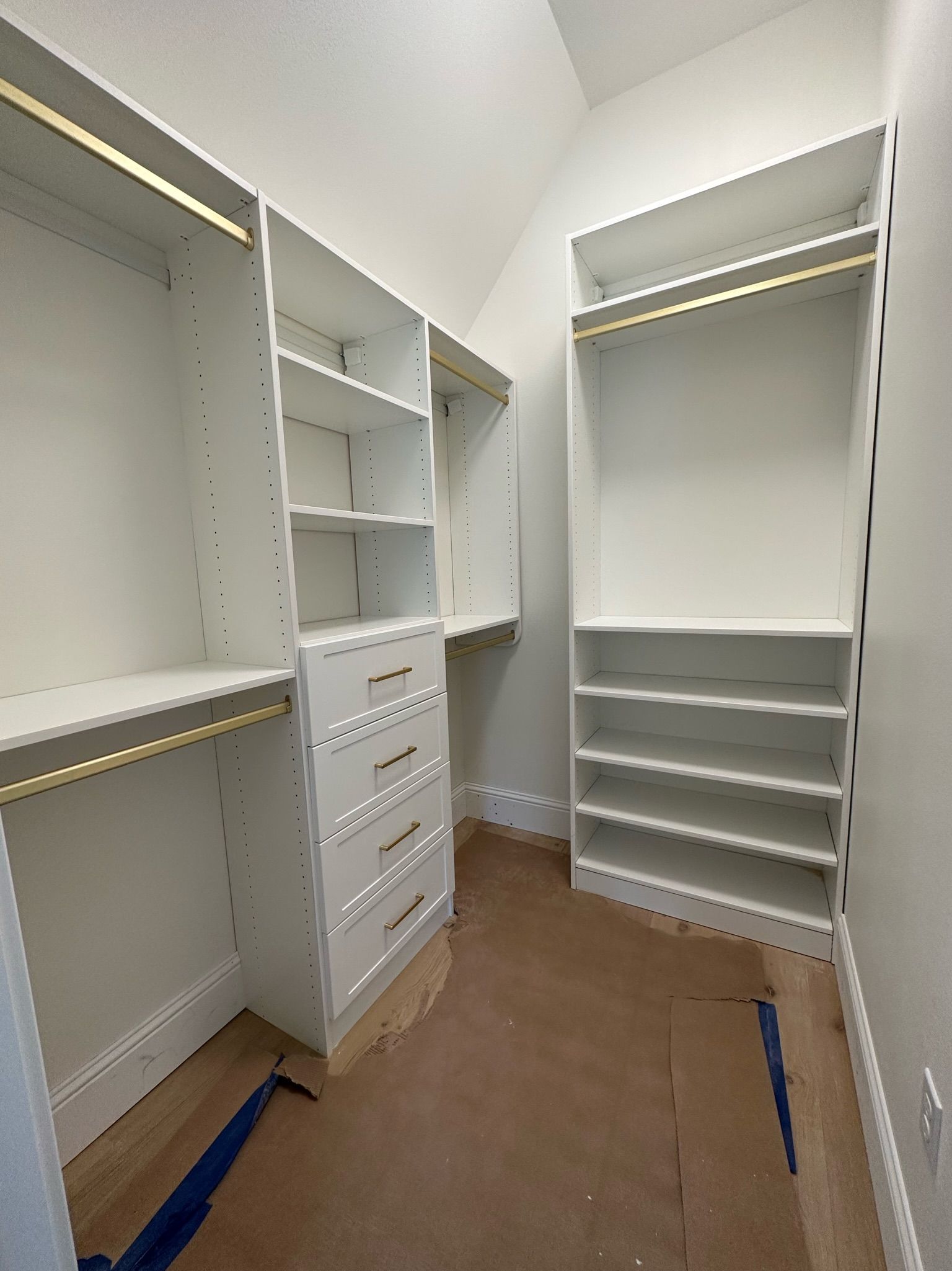 White walk-in closet with shelves, drawers, and hanging rods. Light brown flooring, white walls, angled ceiling.