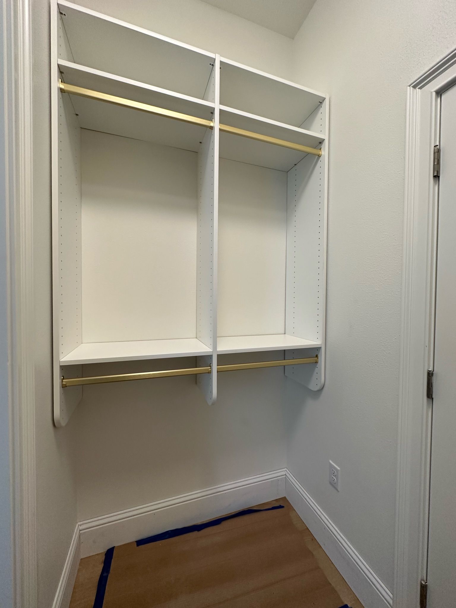 Built-in white closet with shelves and rods, inside a room with a wood floor and a door.