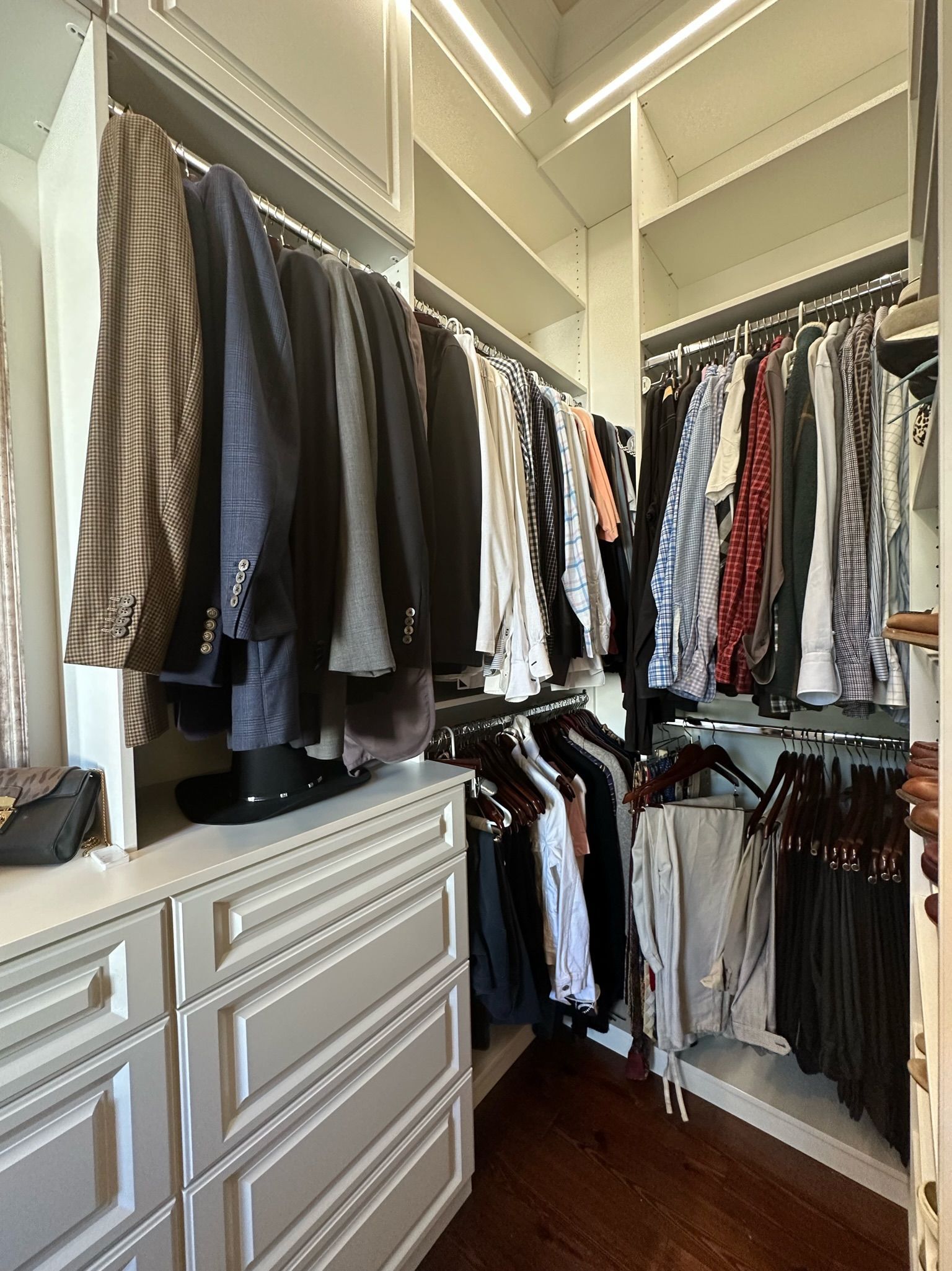 Walk-in closet with drawers, shelves, and hanging clothes, including suits and shirts.