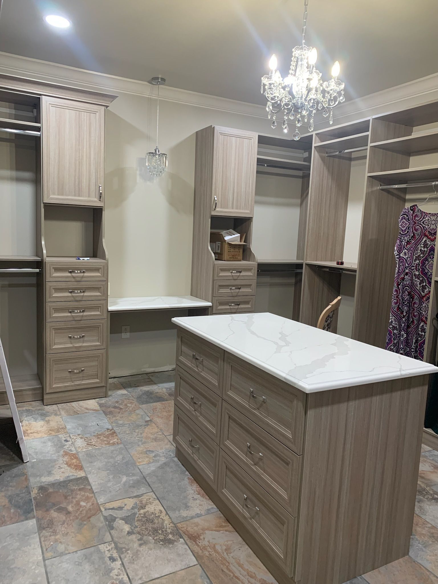 Walk-in closet with custom light brown cabinetry, marble-top island, and chandelier.