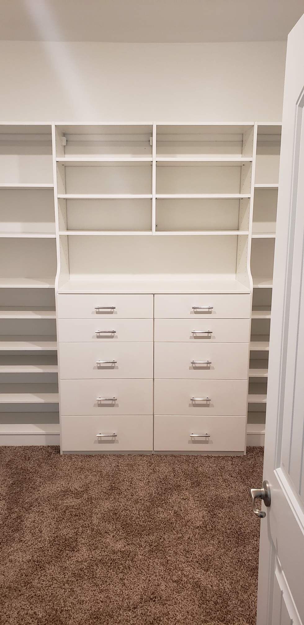 White closet with drawers and shelves in a room with brown carpet. The door frame is visible.