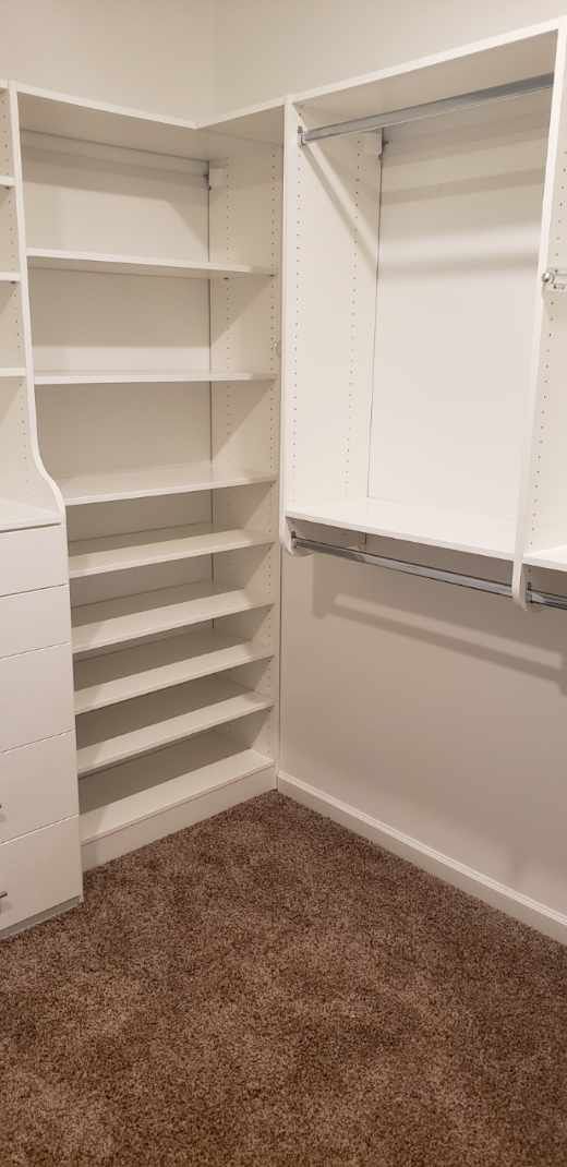 White closet shelving unit with shelves and rods, corner of a room, brown carpet.