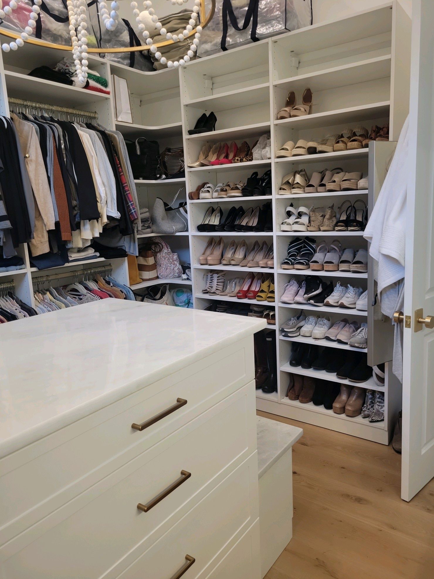 Walk-in closet with shelves of shoes and clothing, white dresser, and light-colored wooden floor.