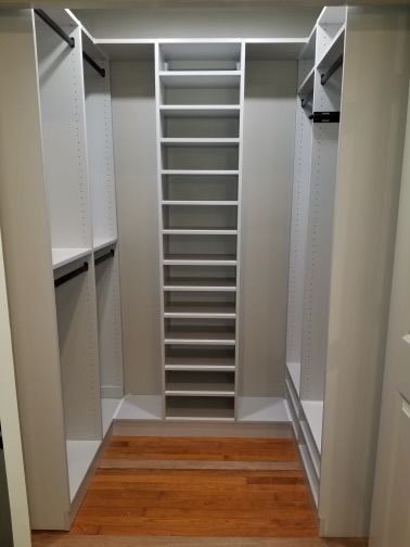 Walk-in closet with white shelving, hanging rods, and a center tower of shelves on wood floor.