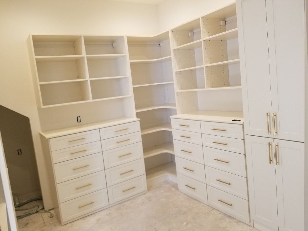 Built-in white closet with shelves, drawers, and tall doors in a room with unfinished flooring.