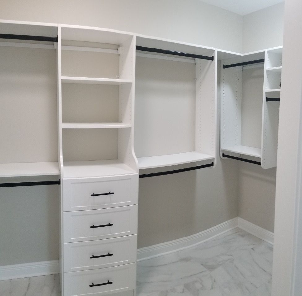 White custom closet with shelves, drawers, and hanging rods. Black handles and rods contrast the white.