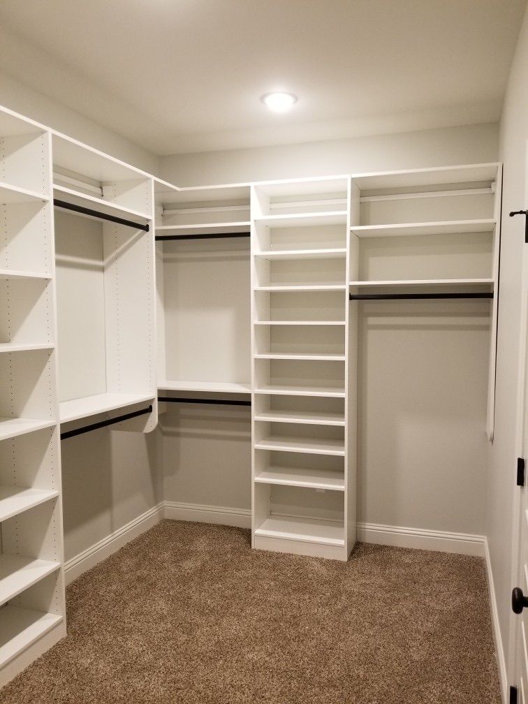 Walk-in closet with white shelving, black rods, tan carpet, and a white ceiling and walls.