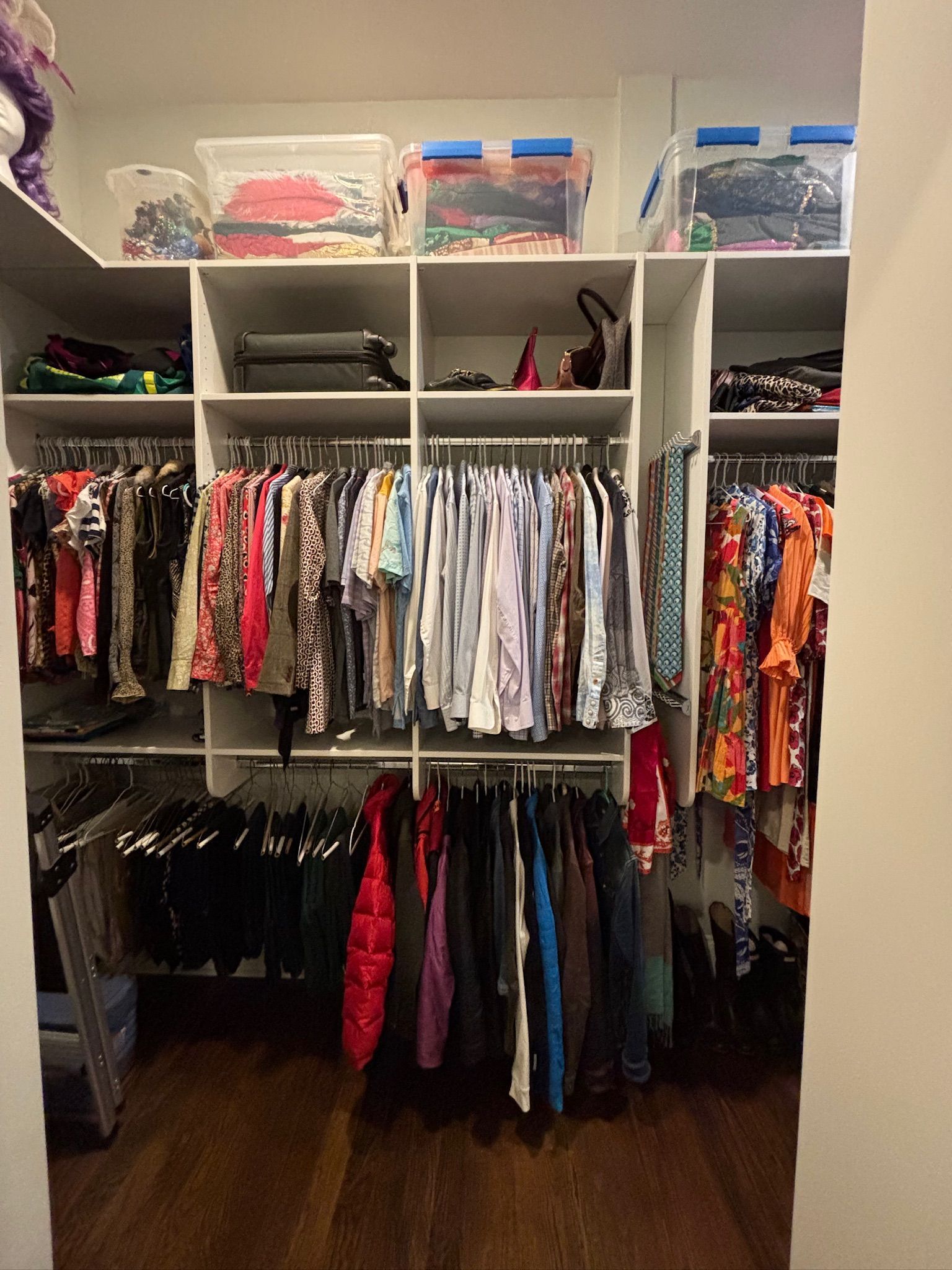 Walk-in closet with clothes on hangers and bins on shelves. Wooden floor.