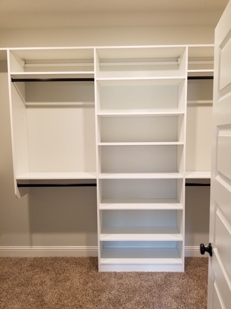 White built-in closet with shelves and hanging rods; light brown carpeted floor; neutral gray walls.