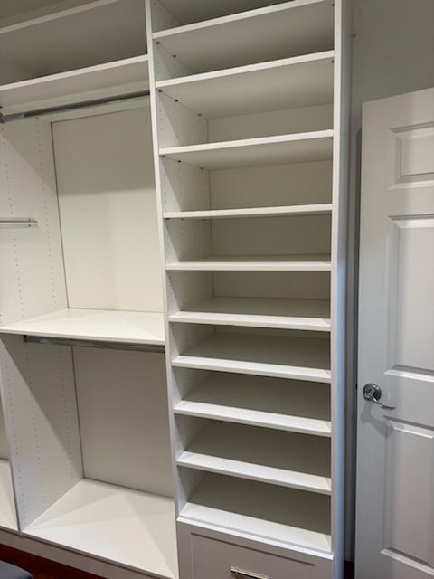 White closet shelving unit with multiple shelves and a drawer. A door is visible on the right.
