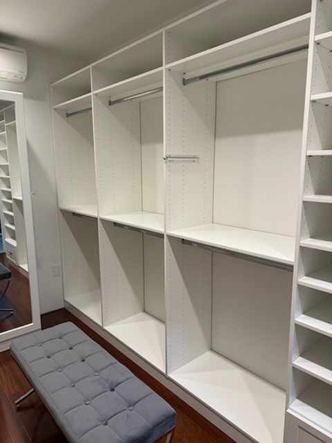 White closet with shelves, rods, and a gray bench.