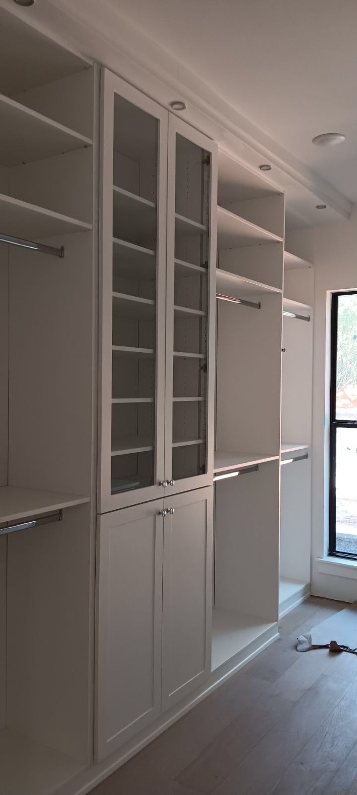 White closet built-in with glass-fronted shelves, hanging rods, and lower cabinet doors.