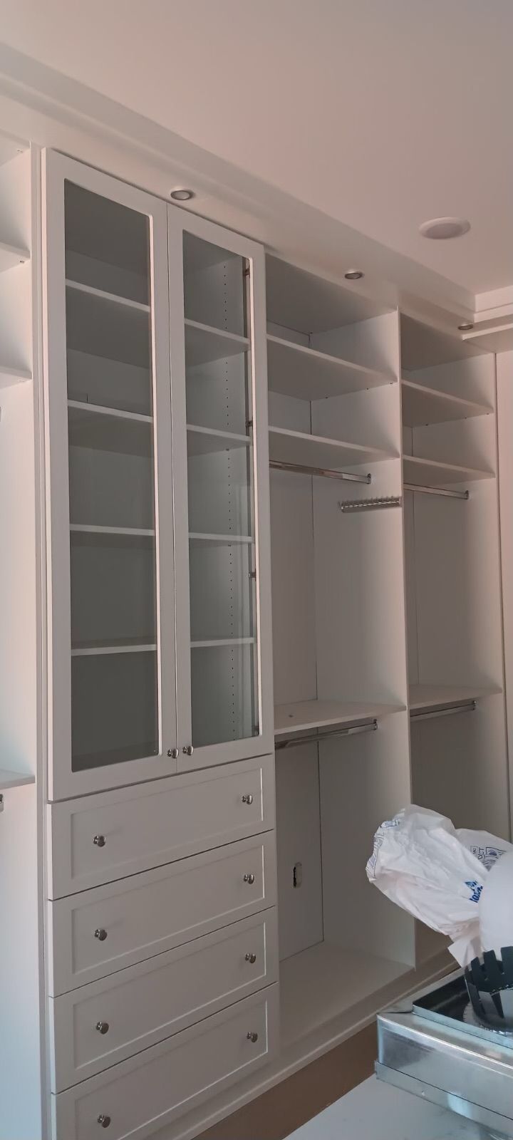 White built-in closet with glass doors, drawers, and hanging rods.