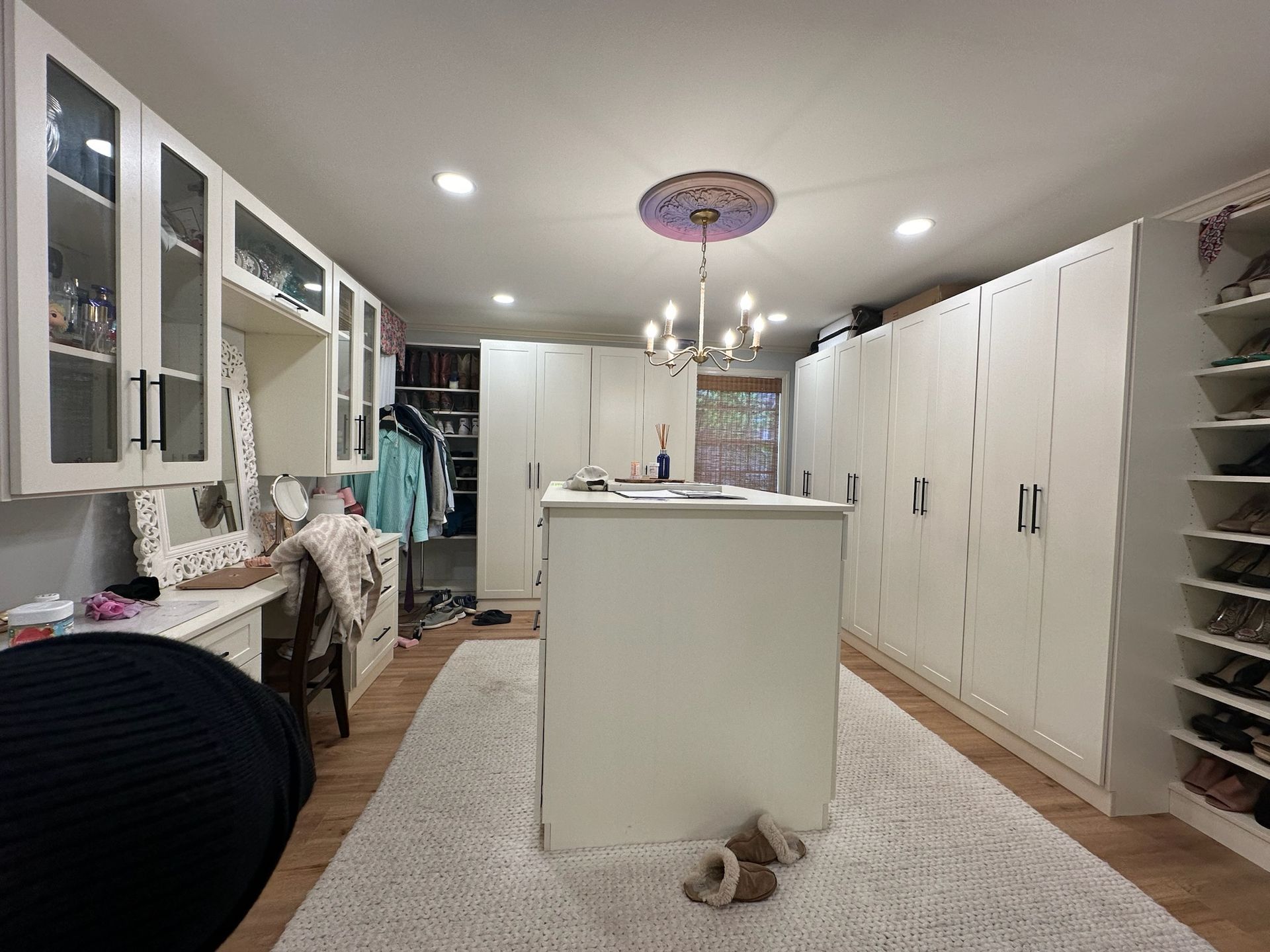 Walk-in closet with white cabinets, a central island, and a rug. Clothes and shoes are visible.