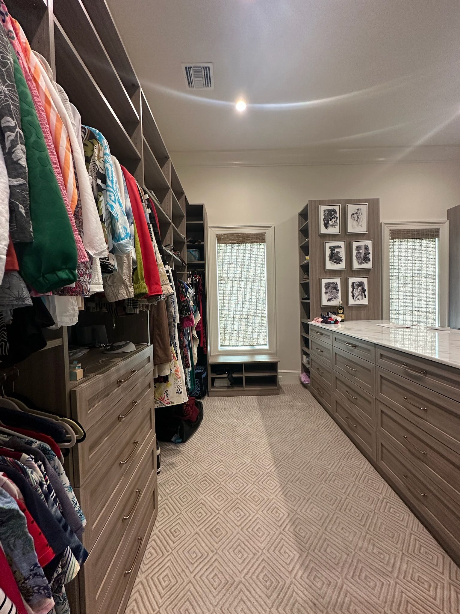 Walk-in closet with clothes, drawers, and a center island with artwork, a window, and patterned carpet.