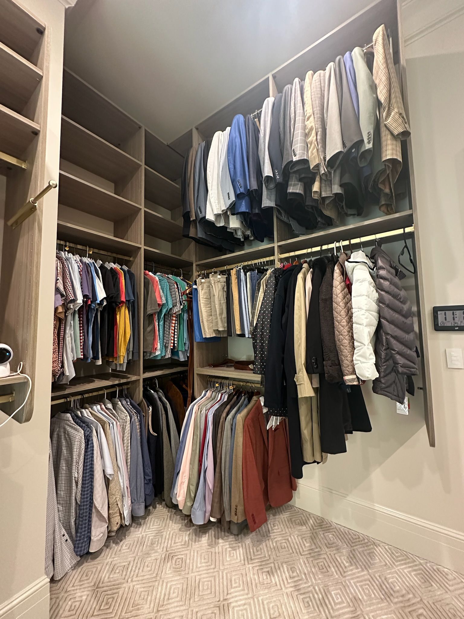 Walk-in closet with clothes hanging on rods and shelves. Neutral tones with a patterned rug.