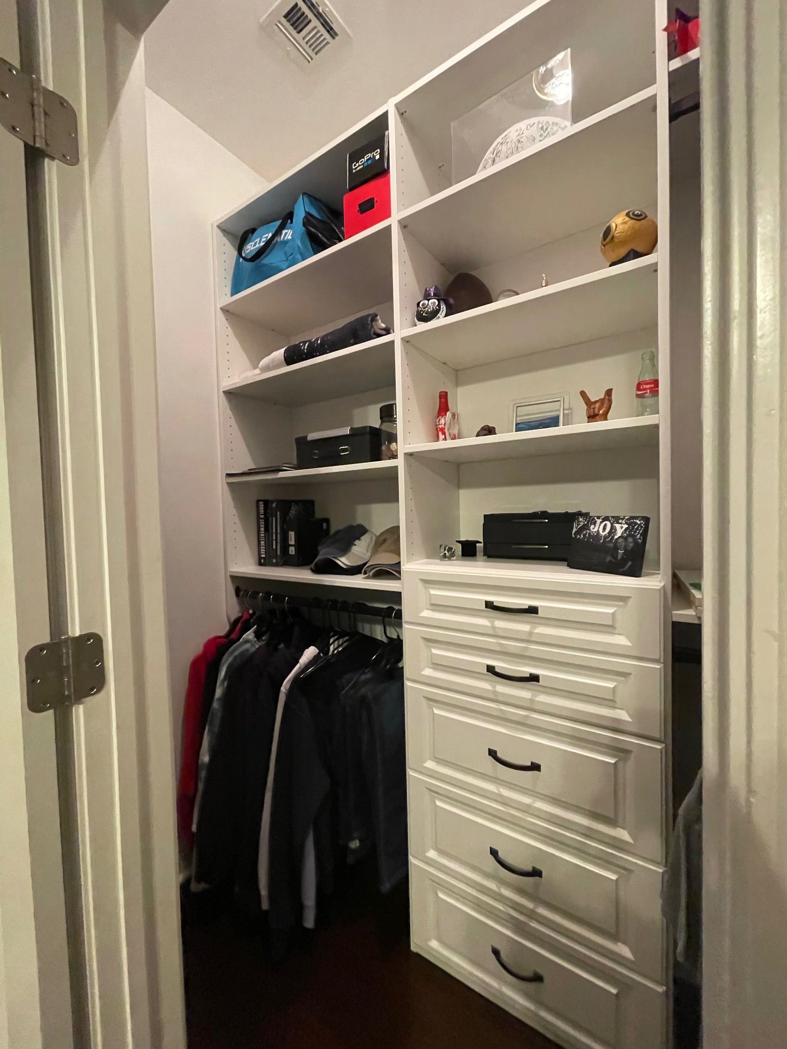 Closet with white shelves and drawers; clothing hangs on a rod.