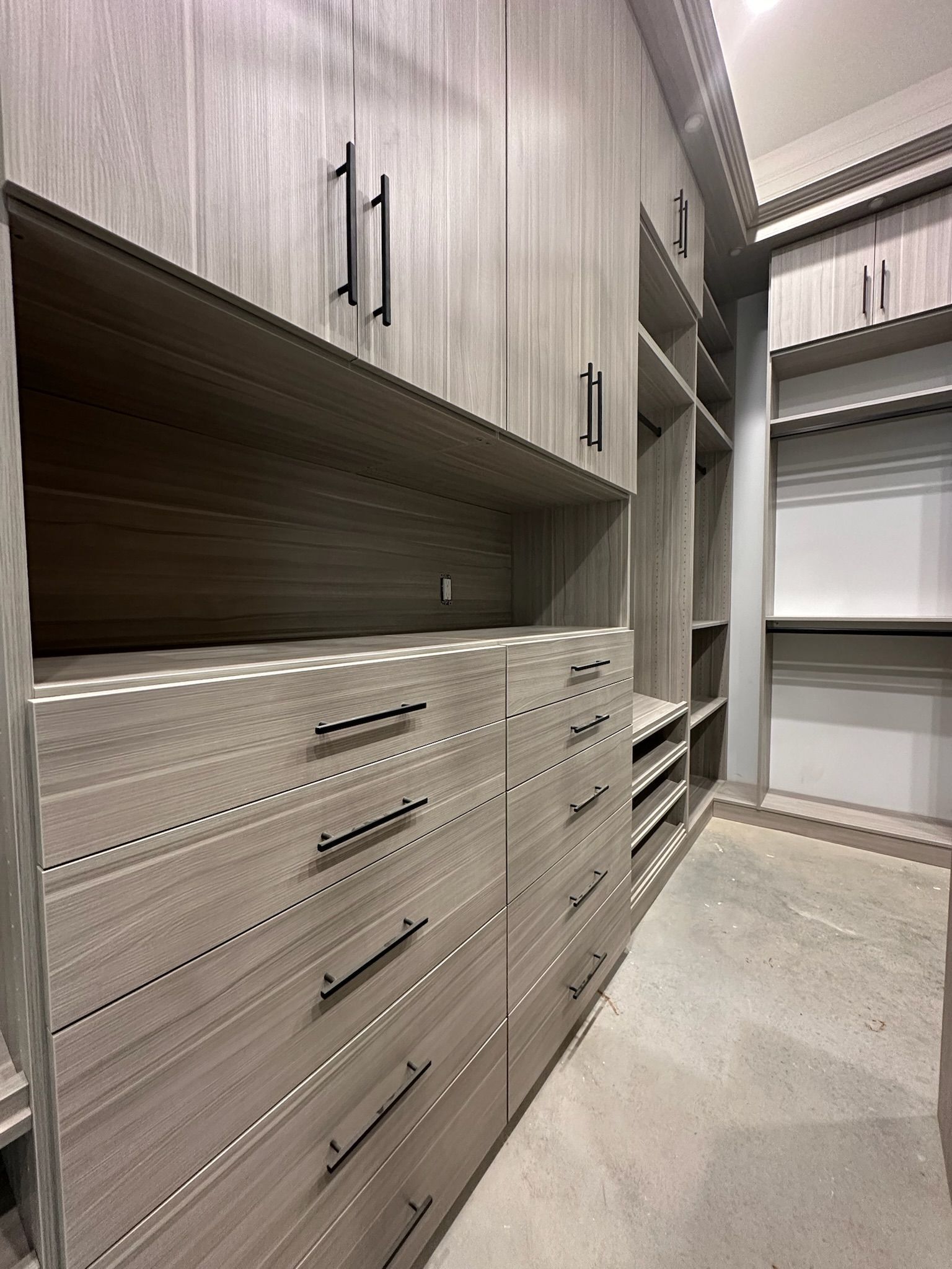 Walk-in closet with gray wood cabinetry, drawers, and shelving; black handles.