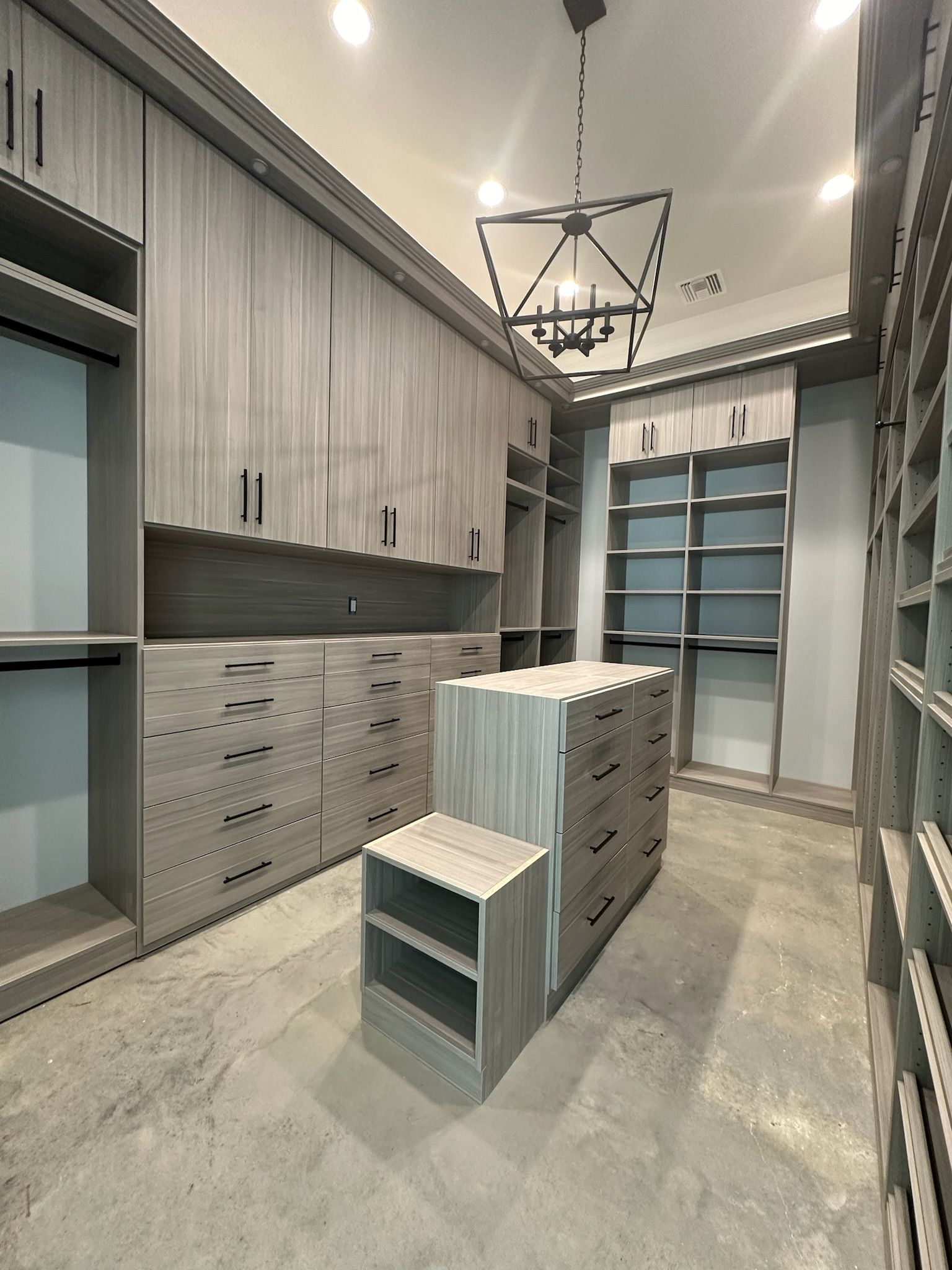 Gray walk-in closet with built-in shelves, drawers, and a central island. A chandelier hangs from the ceiling.