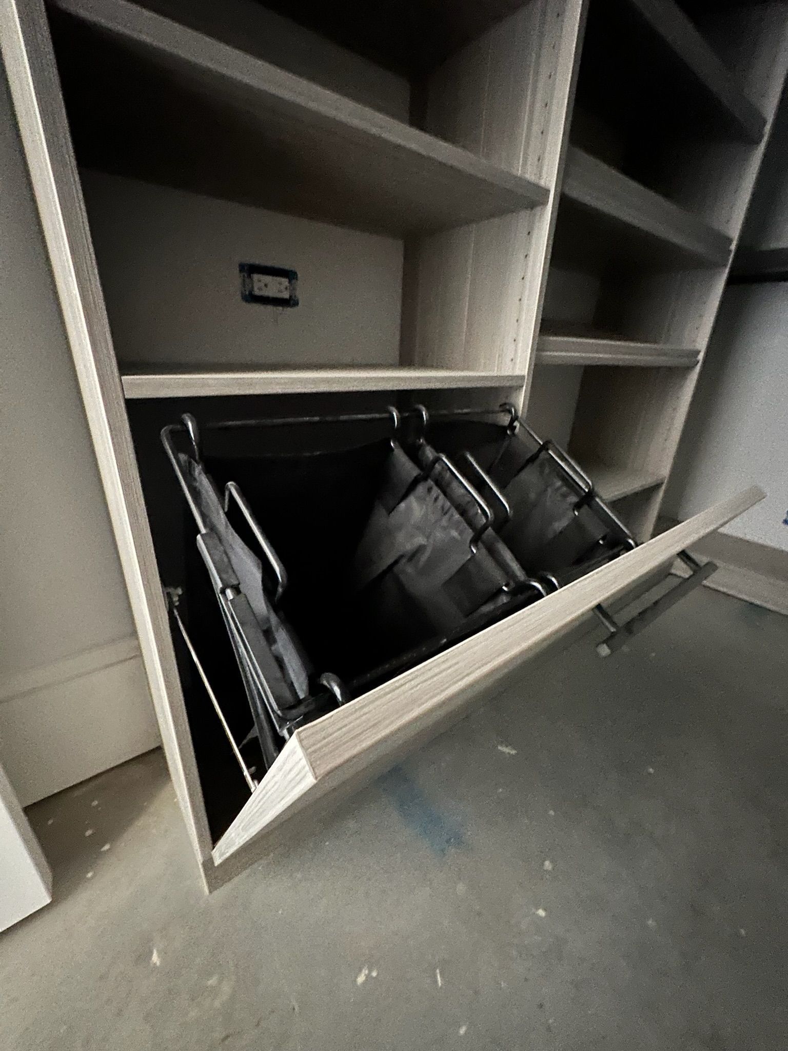 Built-in laundry hamper with two compartments, mounted in a cabinet. The cabinet and hampers are gray.