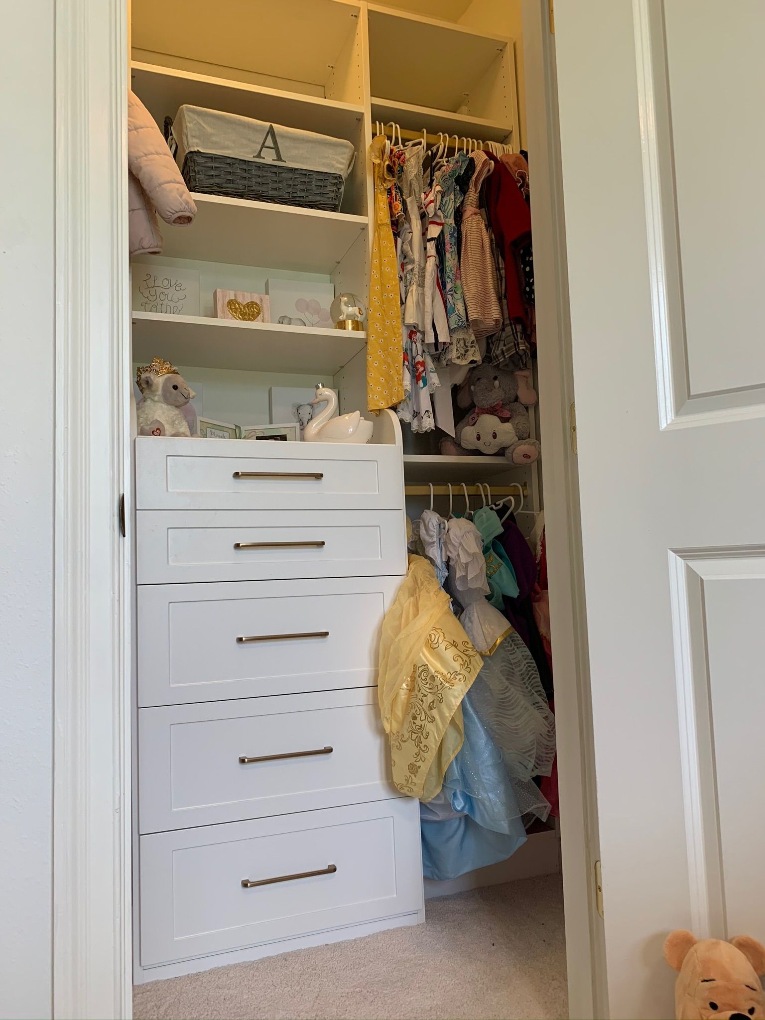 White closet interior with shelves, drawers, and hanging clothes; open door frame.