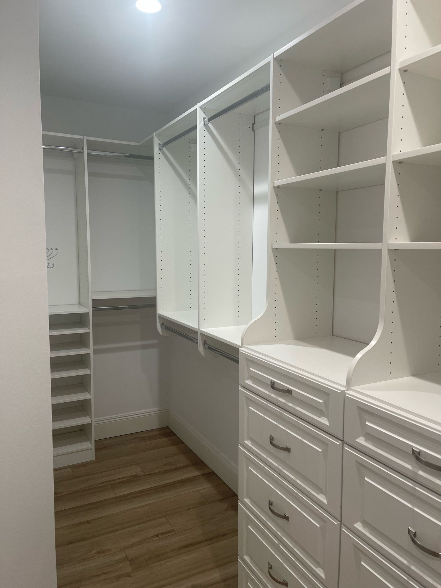 White closet with shelves and drawers, and light wood flooring.