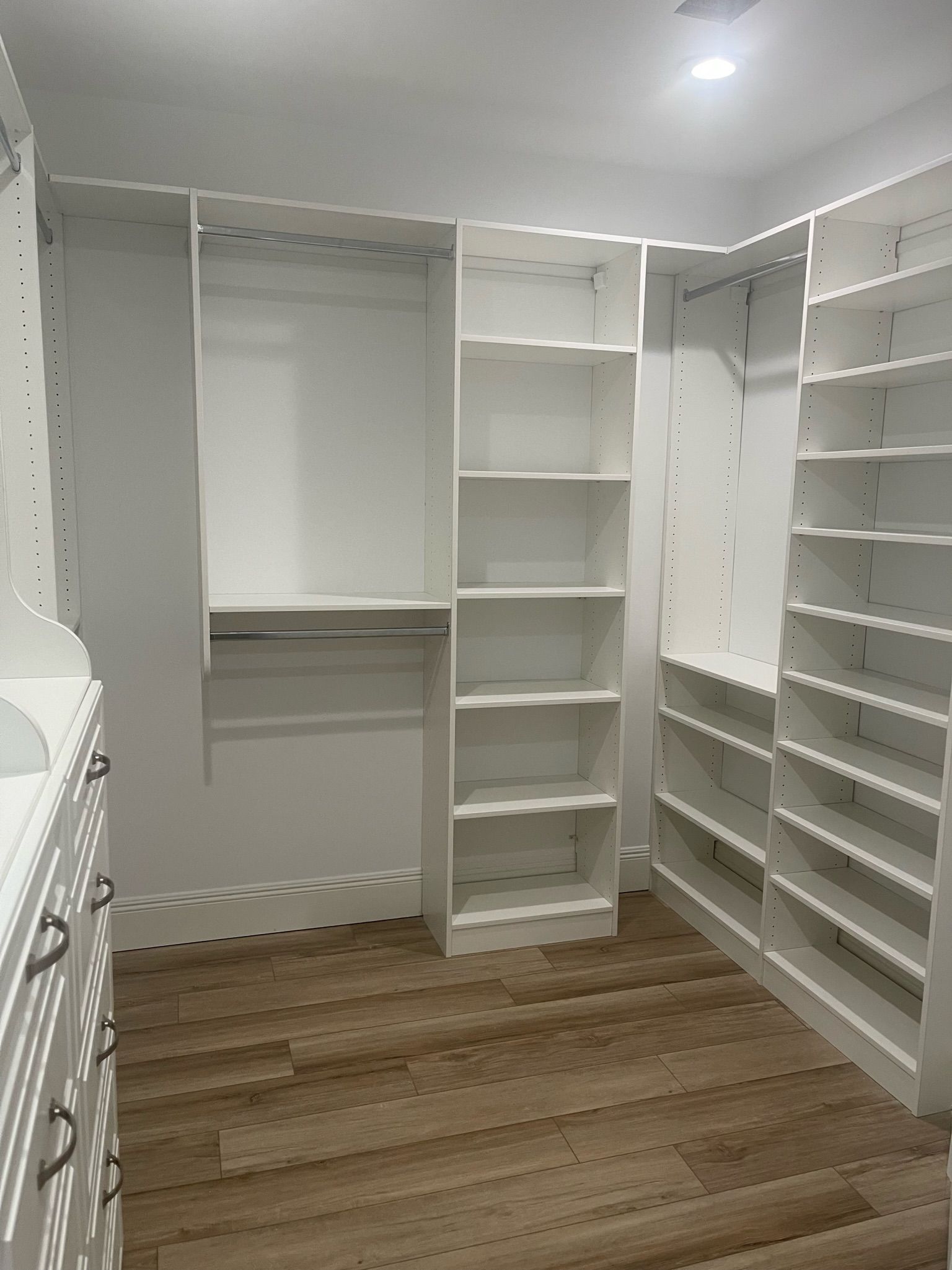 White walk-in closet with shelves and rods, on a wood-look floor.