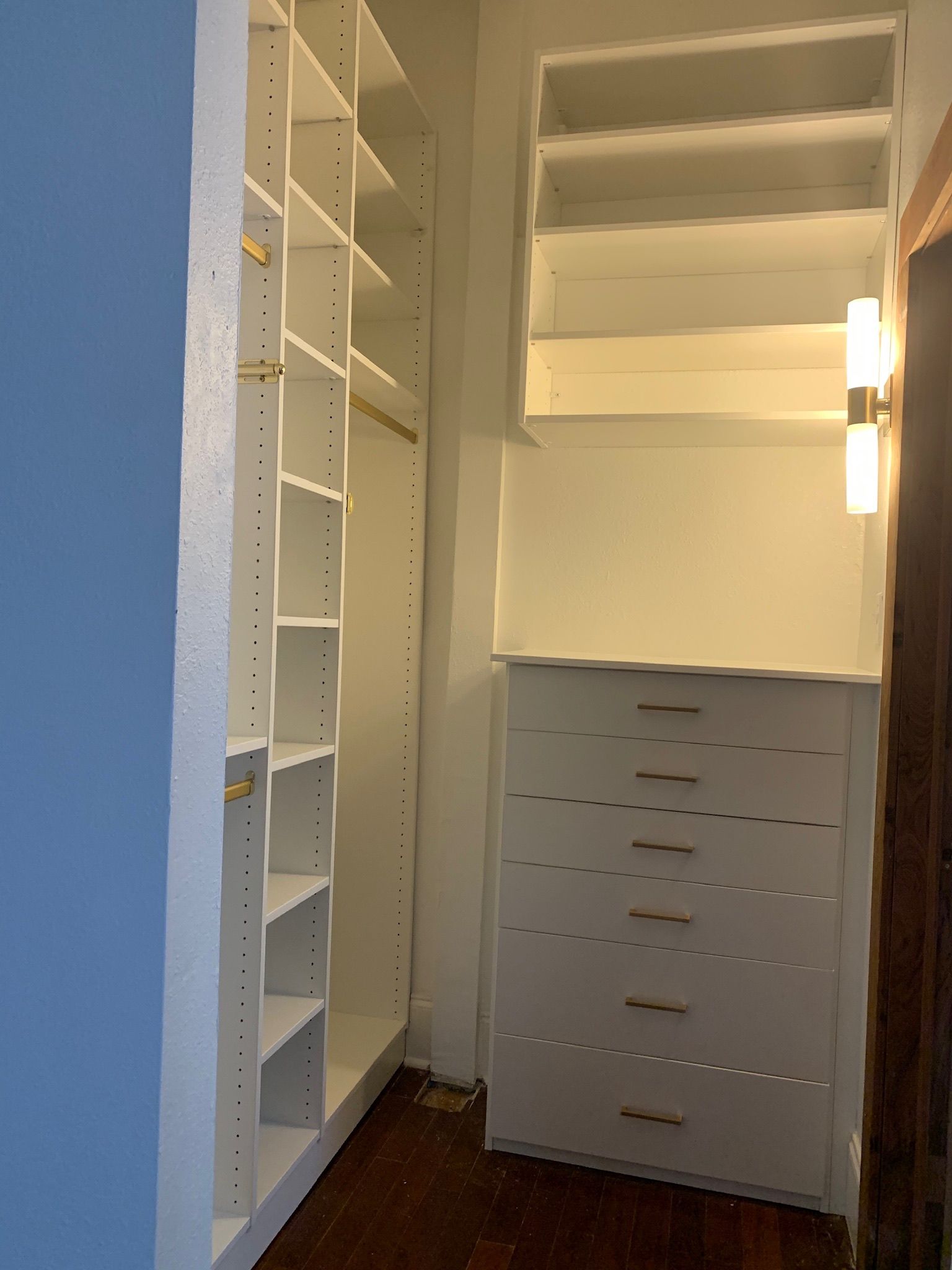 White closet shelving and drawers in a corner, with a light fixture on the side.