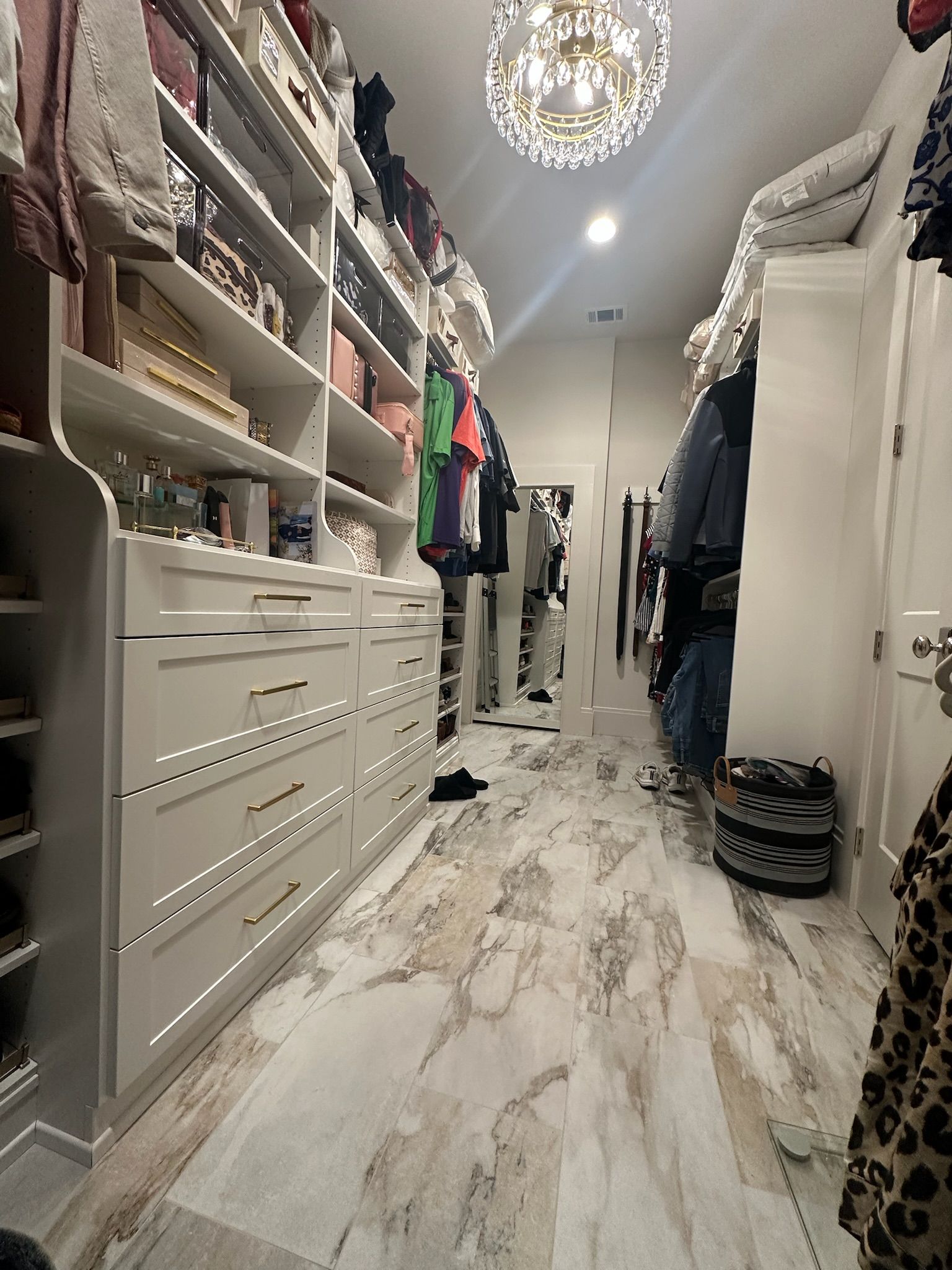 Spacious walk-in closet with white cabinetry, gold hardware, and patterned flooring.
