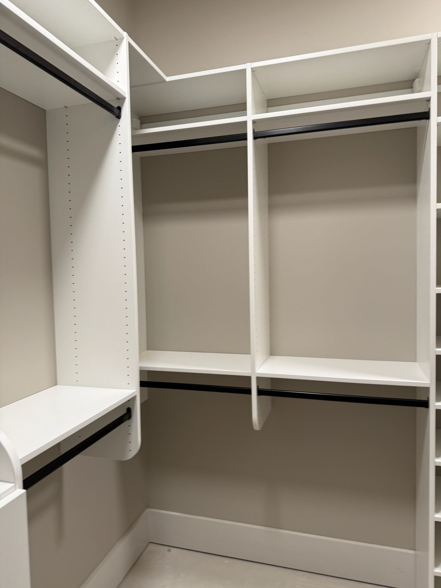 Empty white closet with shelving, hanging rods, and beige walls.