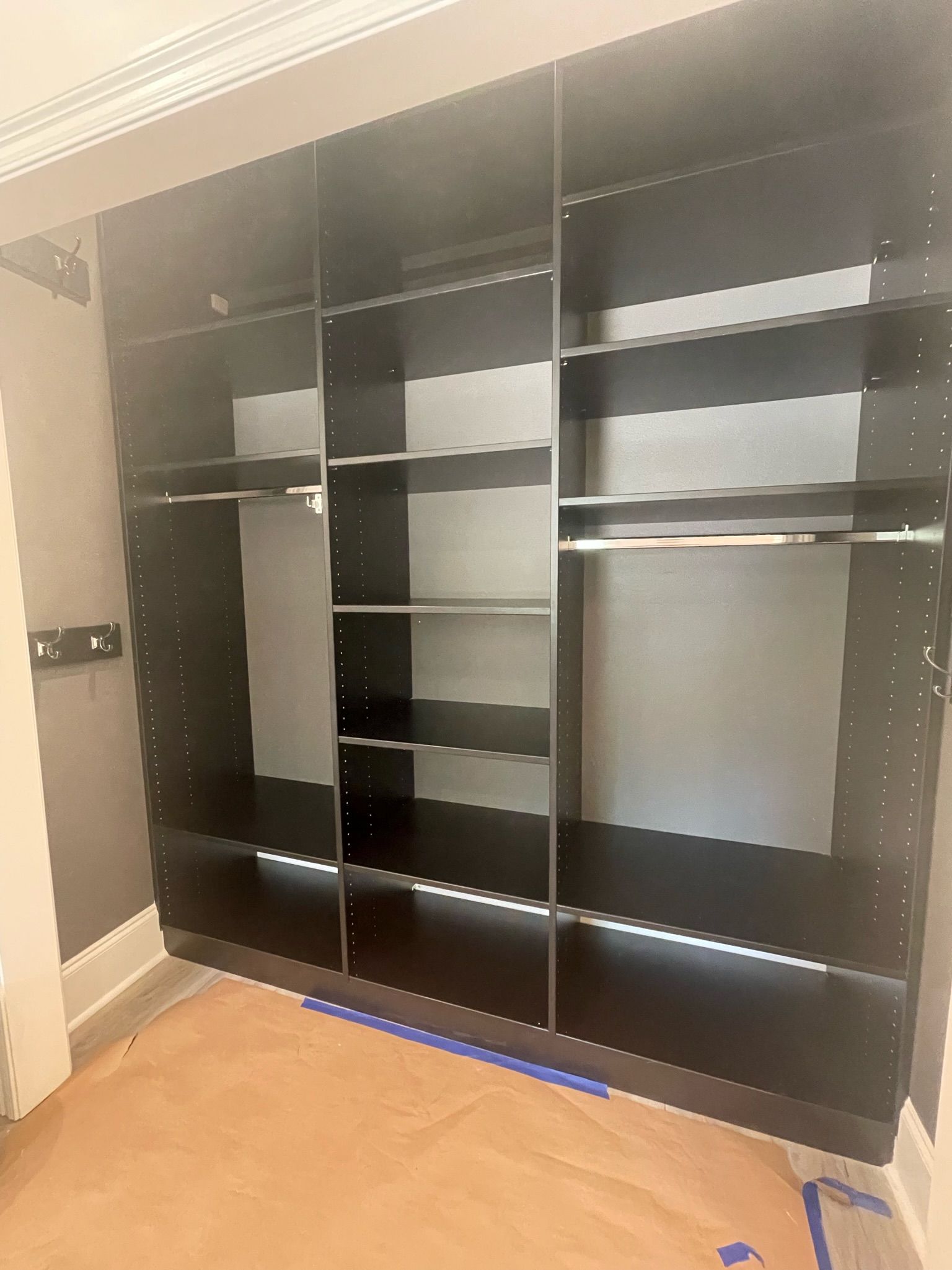 Black closet organizer with shelves and hanging rods, set in a room with light brown flooring.