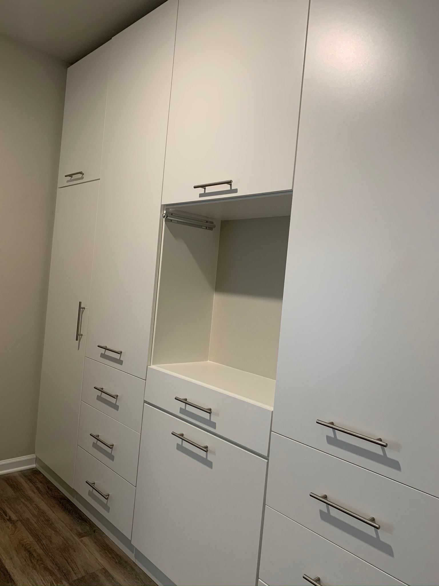 White built-in storage cabinets with drawers and an open shelf area; mounted on a wall with wood-look flooring.