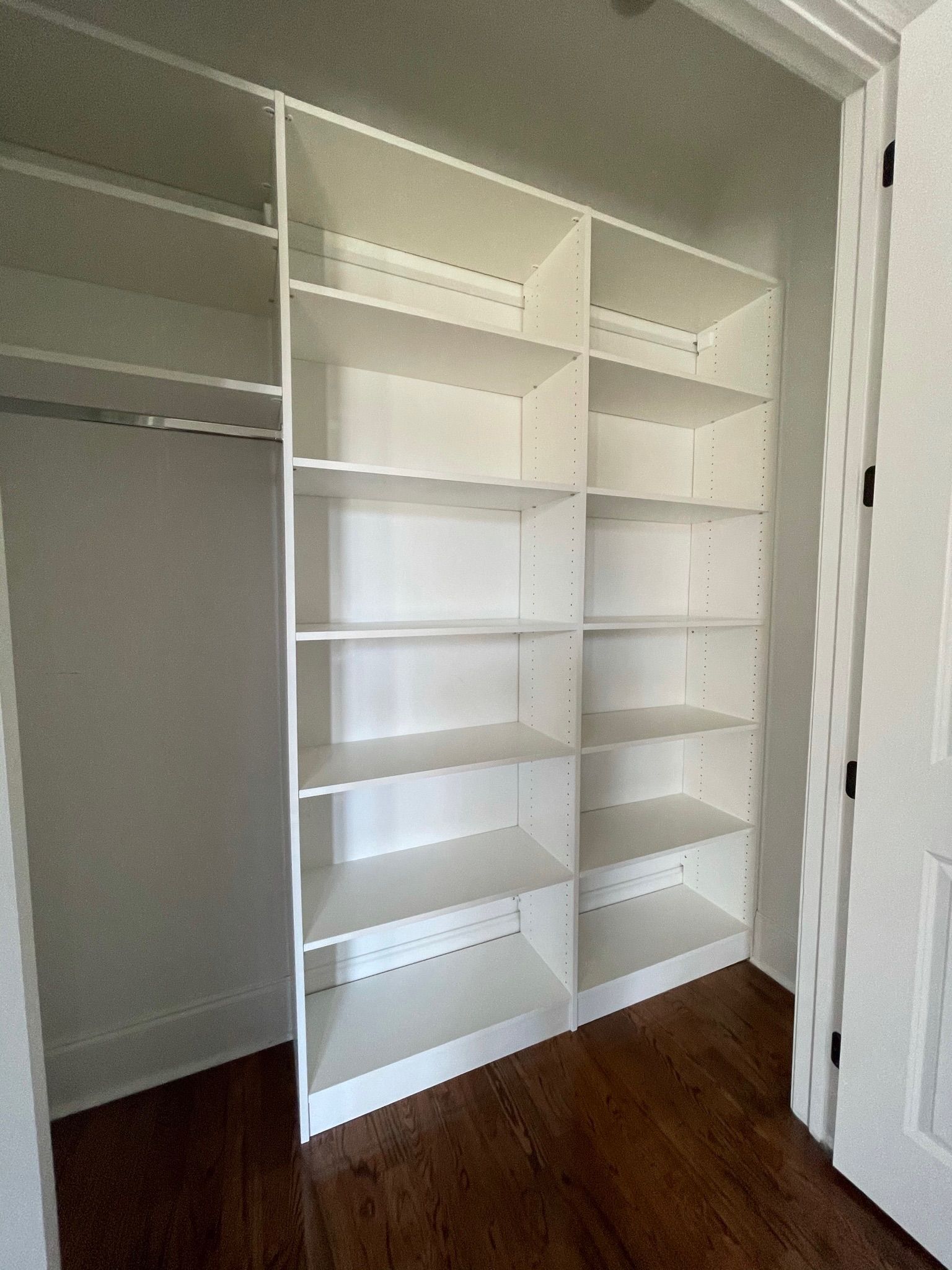 White built-in closet shelving unit with multiple shelves. Dark wooden floor. Doorway on right.