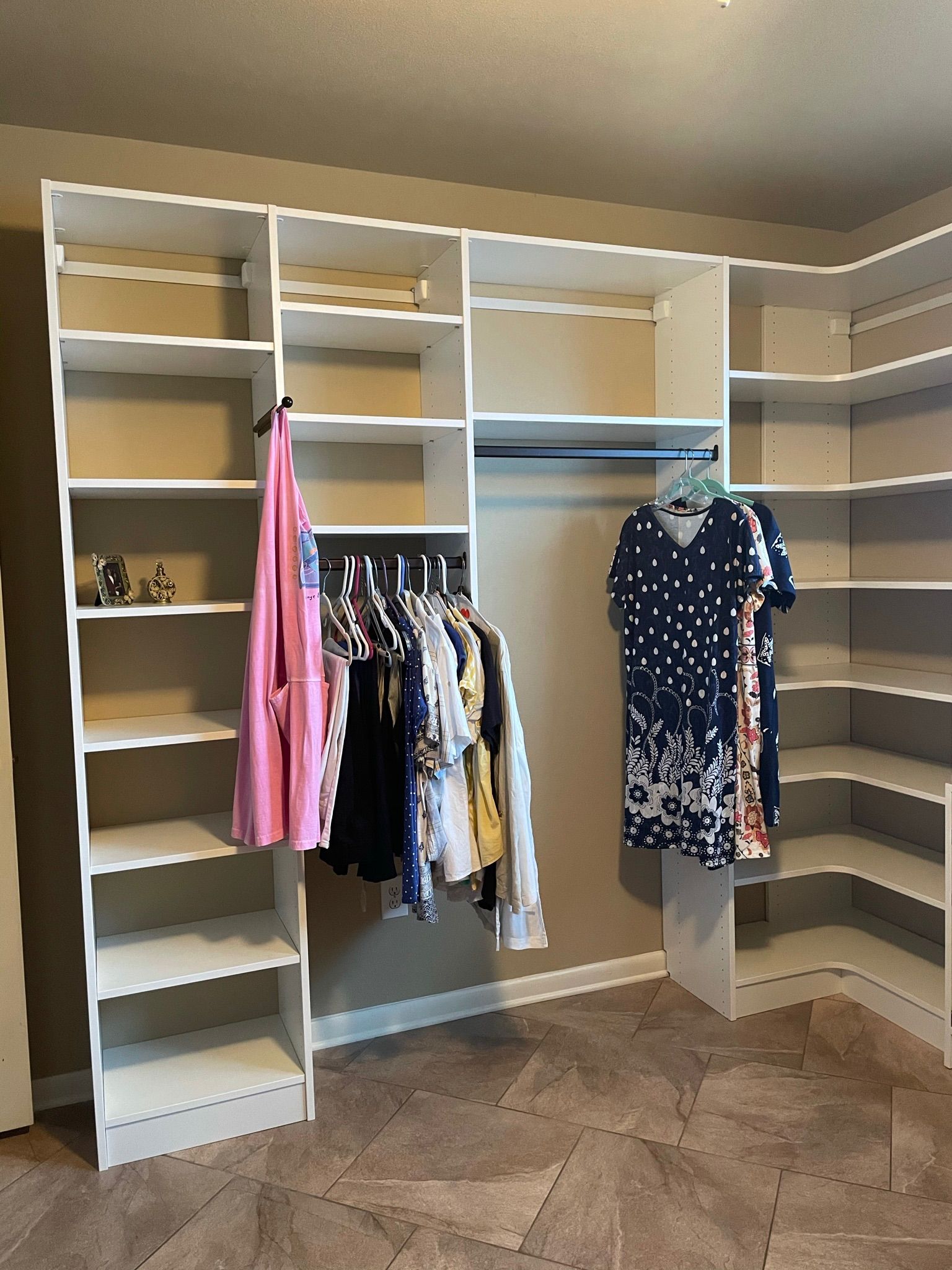White closet organizers with shelves and hanging rods, filled with clothes.