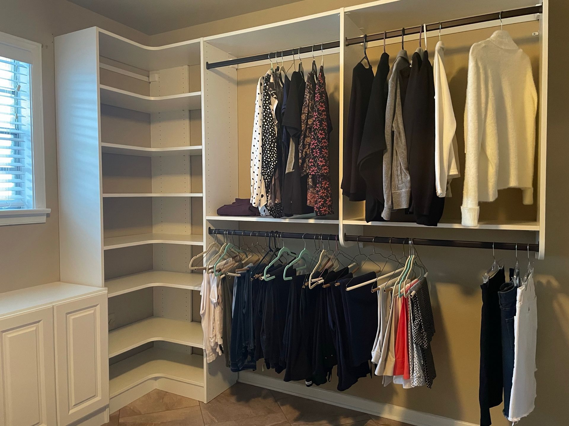 White closet with hanging clothes and shelves; built-in corner shelves and cabinets on the left.