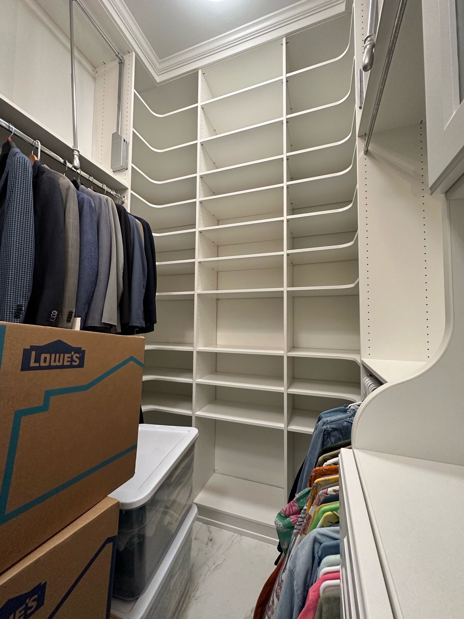 Closet with built-in shelving and hanging rods. Boxes and clothes visible. Mostly white, with beige cardboard boxes.
