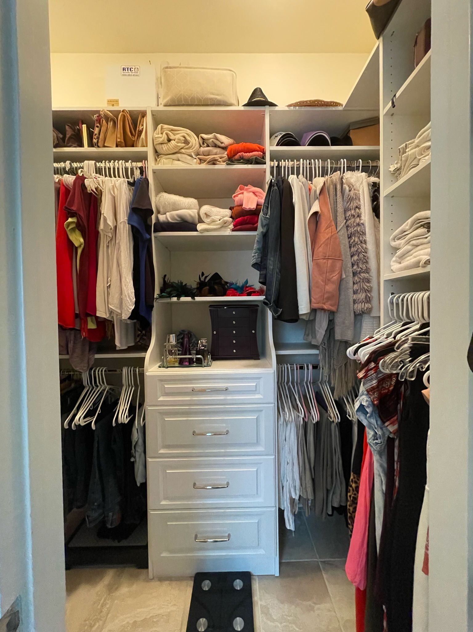 Walk-in closet with white shelves and drawers, filled with hanging clothes, bags, and folded items.