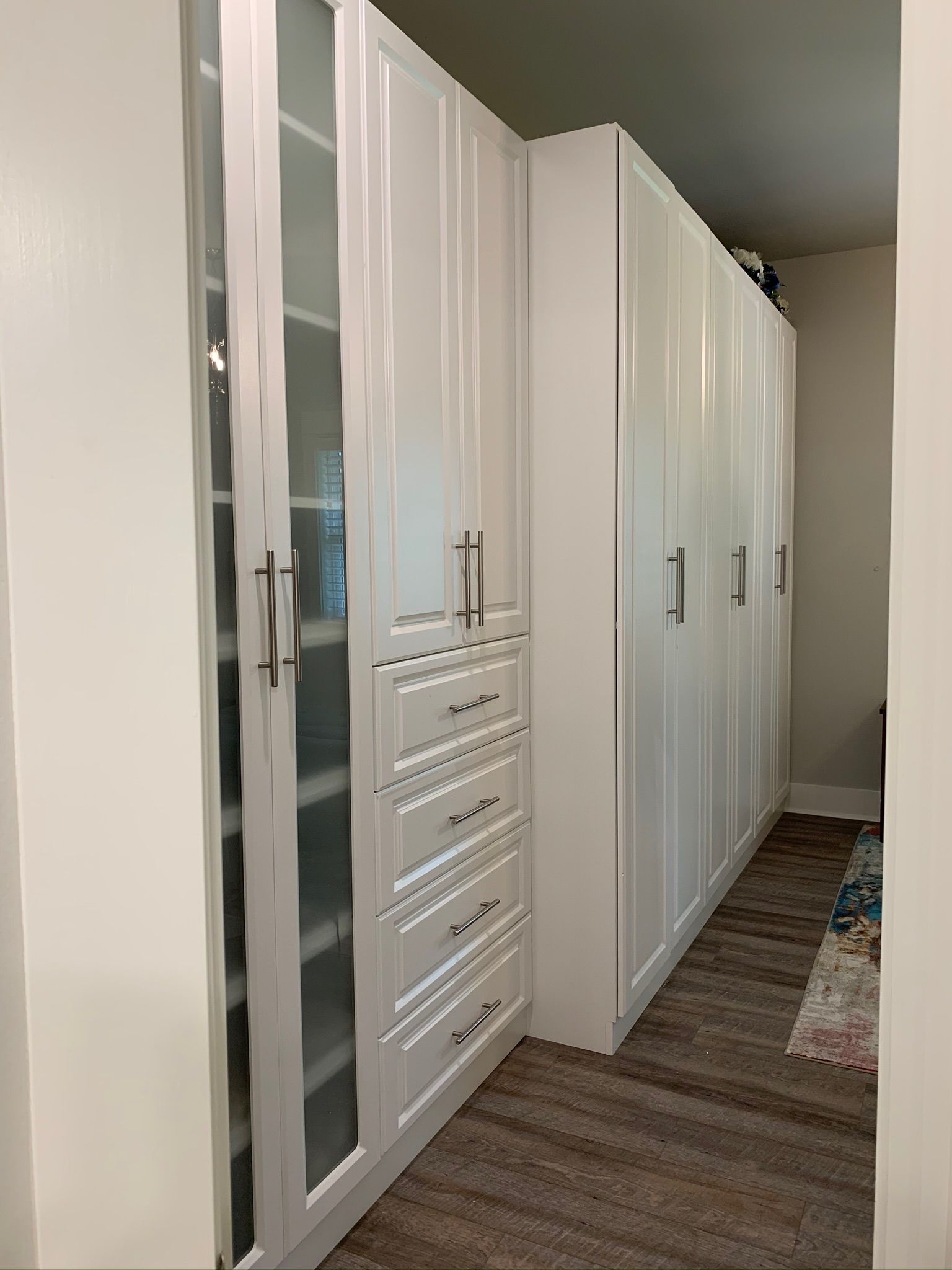 White closet cabinets with glass doors and drawers in a hallway.